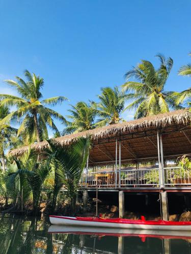a resort with palm trees and a boat in the water at Ba Danh Homestay & Kitchen - Ben Tre Mekong in Ben Tre