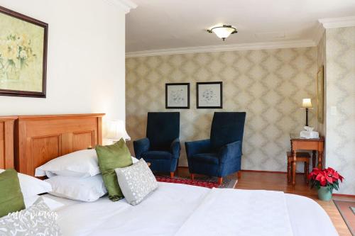 a bedroom with a bed and two blue chairs at A Tuscan Villa Guest House in Fish hoek