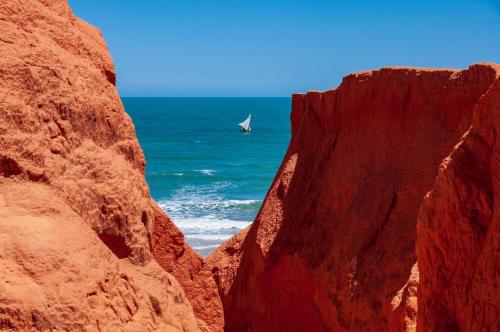 a sail boat in the ocean between two rocks at Hotel Alta Vista in Canoa Quebrada