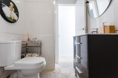 La salle de bains blanche est pourvue de toilettes et d'un miroir. dans l'établissement Mi Bohemia Caleta, à Cadix