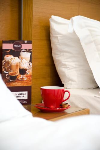 a red coffee cup on a plate next to a bed at Olympion in Athens