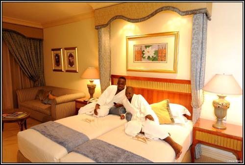 two men sitting on a bed in a hotel room at Peermont D'oreale Grande at Emperors Palace in Kempton Park