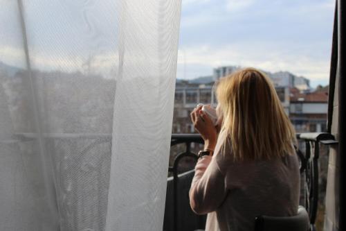 a woman standing on a balcony looking out a window at Hotel Tayko Bilbao in Bilbao