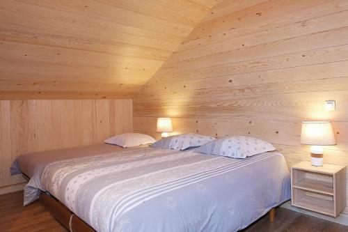 uma cama num quarto de madeira com 2 candeeiros em Le Refuge em Cordon
