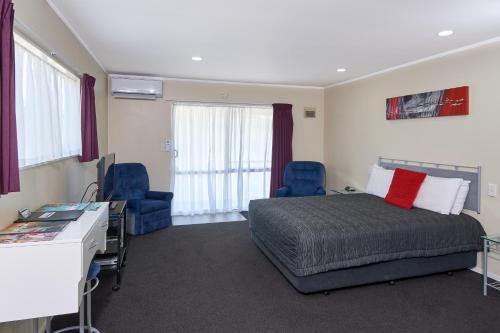 a bedroom with a bed and two chairs and a desk at Livingston Motel in Whakatane