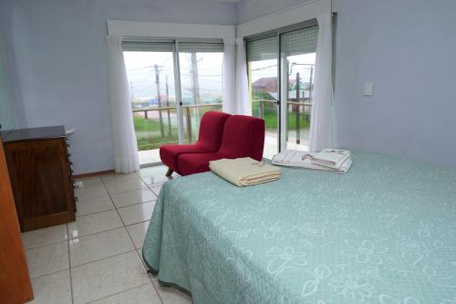a bedroom with a red chair and a bed and a window at Palmas del Caribe in Punta Del Diablo
