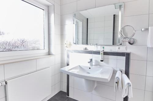 ein weißes Badezimmer mit einem Waschbecken und einem Spiegel in der Unterkunft Hotel & Restaurant Pötter in Emsdetten