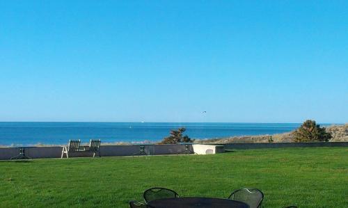 a table and chairs in a field with the ocean at Surf & Sand Beach Motel in South Yarmouth