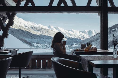 a woman sitting at a table looking out a window at mountains at Mooser Hotel in Sankt Anton am Arlberg