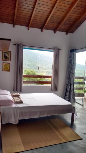 a bedroom with a bed and a large window at La Casa Rozada Prumirim in Ubatuba