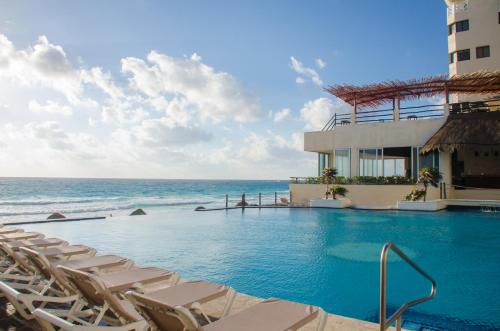 a swimming pool next to the ocean with lounge chairs at BSEA Cancun Plaza Hotel in Cancún