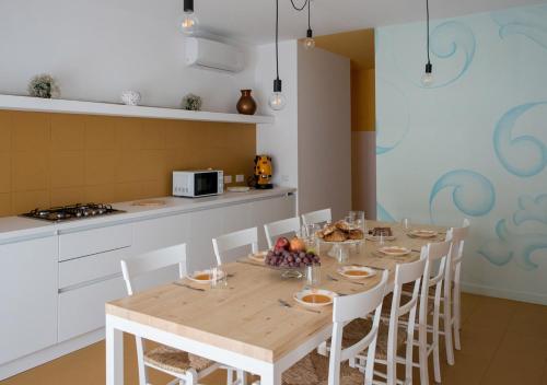 una cucina con un tavolo di legno e sedie bianche di Oikos Selinunte Guest House a Marinella di Selinunte