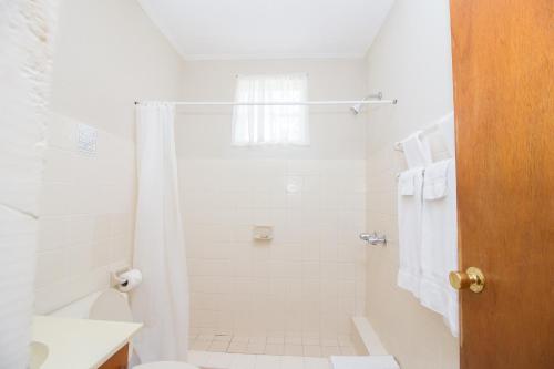 La salle de bains blanche est pourvue d'une douche et de toilettes. dans l'établissement Rosewood Apartment Hotel, à Arnos Vale