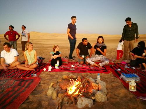 a group of people sitting around a fire in the desert at Queen Desert camp in Fulayj al Mashāʼikh
