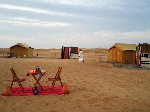 a person walking in the desert with two chairs and a blanket at Queen Desert camp in Fulayj al Mashāʼikh