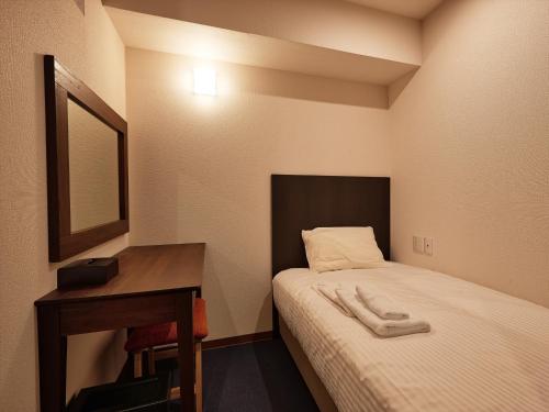a small room with a bed and a desk at Creass Hotel Tsubogawa Marche in Naha