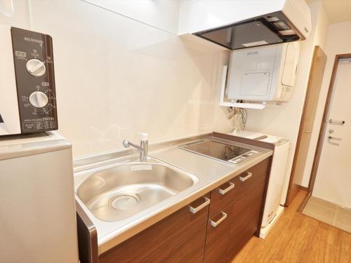 a small kitchen with a sink and a refrigerator at Creass Hotel Tsubogawa Marche in Naha