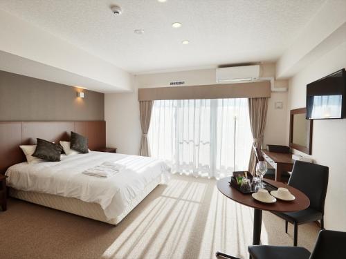 a bedroom with a bed and a table and a television at Creass Hotel Tsubogawa Marche in Naha