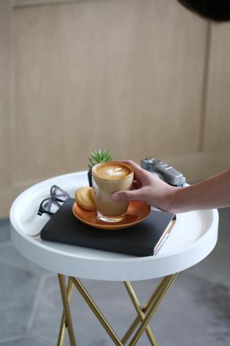 a person holding a cup of coffee on a table at Kampi Hotel Tunjungan - Surabaya in Surabaya