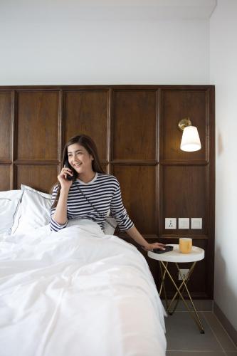 a woman sitting in bed talking on a cell phone at Kampi Hotel Tunjungan - Surabaya in Surabaya