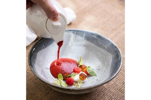 a person pouring strawberry sauce into a bowl of food at Cape Fahn Hotel - Private Islands Samui in Choeng Mon Beach