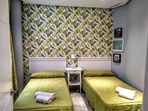 dwa łóżka w pokoju z tapetą w obiekcie Apartamentos El Vestuario w Kadyksie