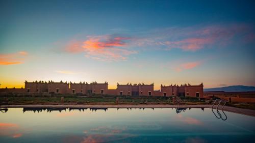 a sunset over a building with a pool of water at Ecolodge l'île de Ouarzazate in Ouarzazate