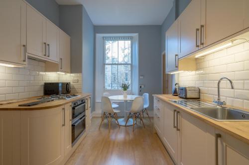 エディンバラにあるEdinburgh Serviced Apartmentのキッチン(白いキャビネット、テーブル、椅子付)