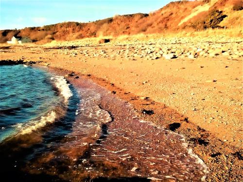 a beach with rocks and water and a mountain at Sea Song, Selkie House in Helmsdale