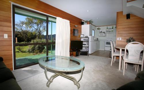 a living room with a glass table and a kitchen at Capeview Cottage in Opotiki