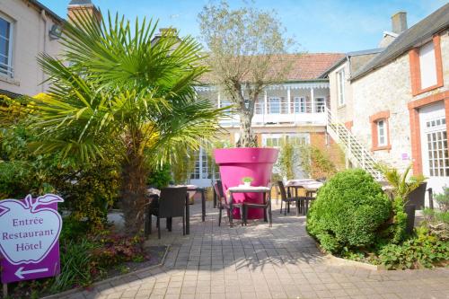 a patio with pink chairs and tables in a courtyard at Logis Hôtel Restaurant l'Auberge Normande in Carentan