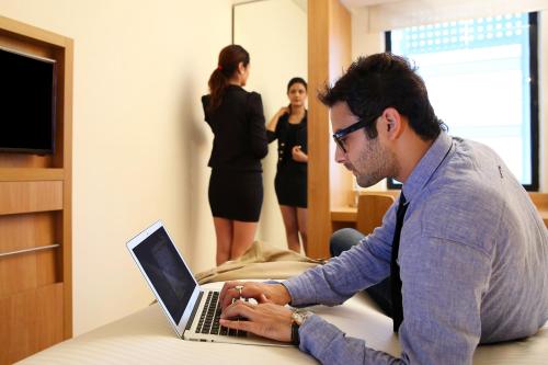 a man sitting on a bed using a laptop computer at ibis Chennai City Centre - An Accor Brand in Chennai