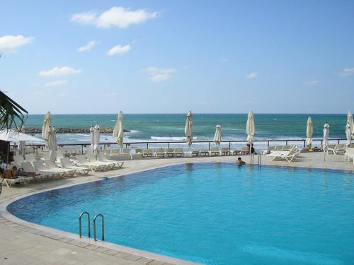 a swimming pool next to the beach with chairs and umbrellas at Raphael Apartments in Herzelia 