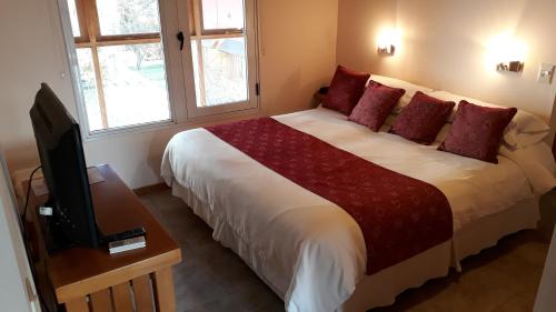 a bedroom with a large bed with red pillows and a television at Hotel Antiguos in San Martín de los Andes