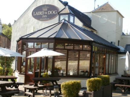 a restaurant with tables and umbrellas in front of a building at Laird And Dog Inn in Lasswade