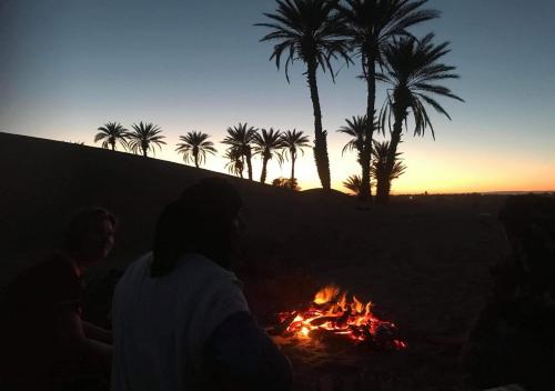 a group of people sitting around a campfire with palm trees at Auberge L'Oasis Mhamid in Mhamid