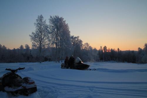a group of people standing in the snow with a snowmobile at Maatilamatkailu Jänisvaara in Kolinkylä