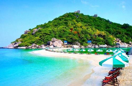 a beach with umbrellas and chairs and a mountain at Nangyuan Island Dive Resort in Koh Tao