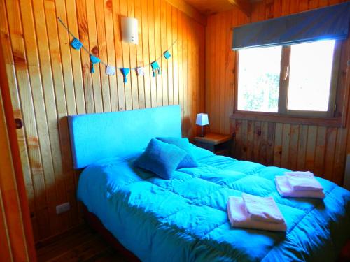 1 dormitorio con cama con sábanas azules y ventana en Casita de Madera en San Carlos de Bariloche