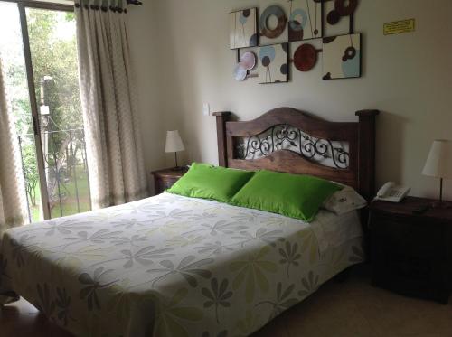 a bedroom with a bed with green pillows and a window at Hotel Castellana Inn in Bogotá