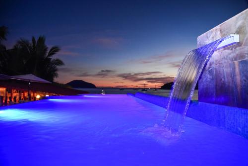 a swimming pool with a water fountain at night at Arena Suites in Zihuatanejo