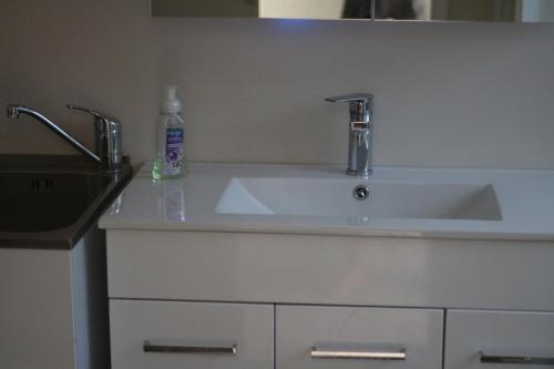 a white sink with two faucets and a bottle of soap at Beach across the road in Waihi Beach