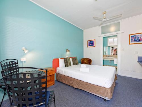 a room with a bed, chair, table and a lamp at Riviera Motel Bundaberg in Bundaberg