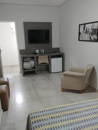a living room with a television and a desk with a chair at Hotel Ouro Verde in Três Pontas