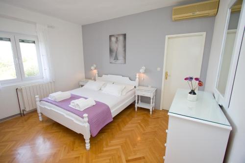 a white bedroom with a white bed and a wooden floor at Apartment Glavina with private pool in Makarska