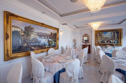 カステッランマーレ・ディ・スタービアにあるLa Panoramica Hotelの白いテーブルと椅子、絵画が飾られたダイニングルーム
