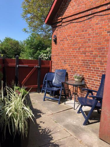 a patio with chairs and a table and a brick wall at Det lille røde hus in Nyord