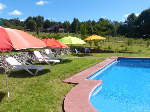 una piscina con sombrillas, sillas de césped y sombrillas en Cabañas Domo Pucón en Pucón