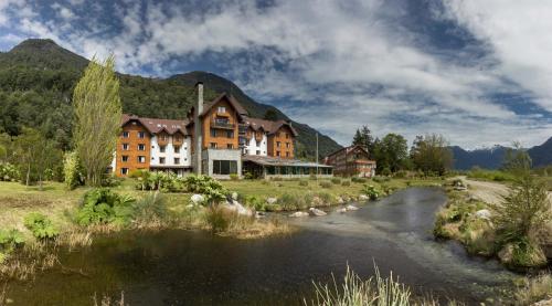 a building with a river in front of a mountain at Hotel Natura in Peulla