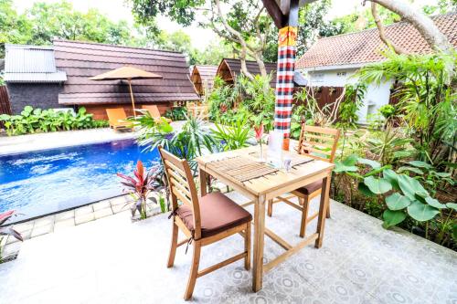 a wooden table and chairs next to a swimming pool at Kubu Kak Dudung Villas in Jimbaran